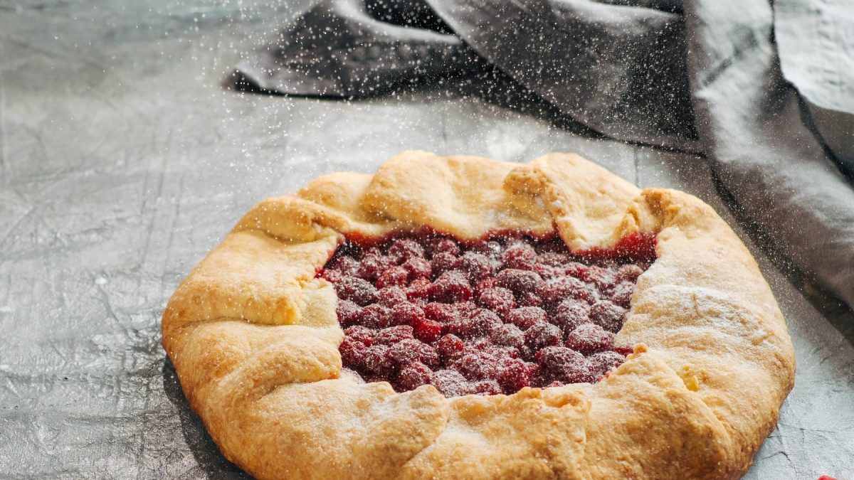 Die Galette mit Cranberrys auf einem grauen Untergrund. Die gAlette wird mit Puderzucker bestäubt.