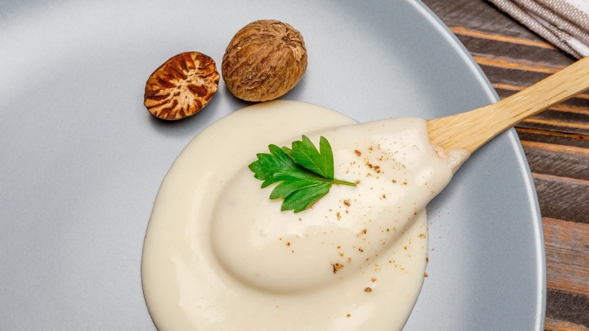 Ein blaugrauer Teller mit Béchamel-Sauce neben Muskatnuss.