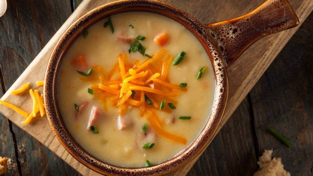Eine braune Schüssel mit Bier-Käse-Suppe auf einem Holzbrett.