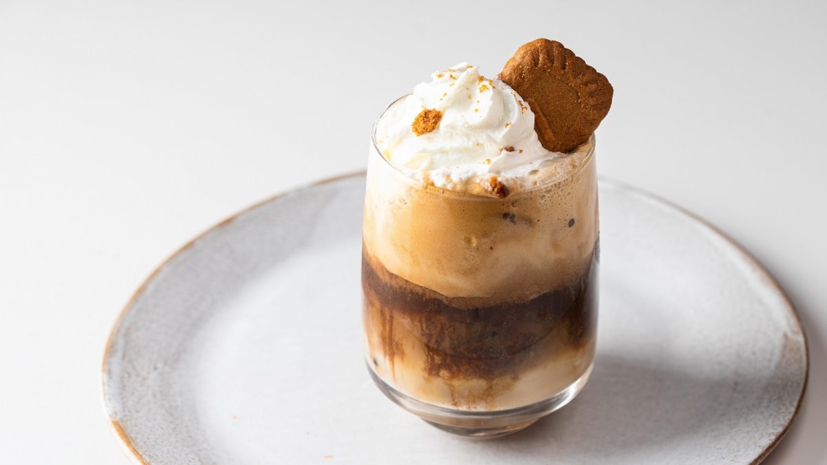 Ein Glas mit Lotus Biscoff Latte auf einem weißen Teller.