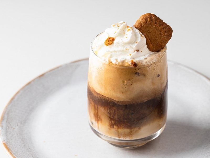 Ein Glas mit Lotus Biscoff Latte auf einem weißen Teller.
