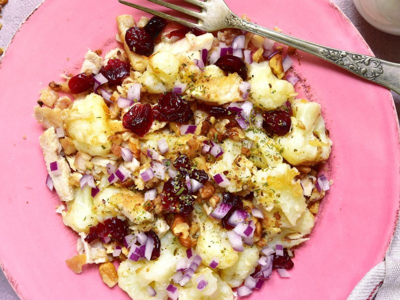 Ein rosa Teller mit Blumenkohl-Salat mit Cranberries.