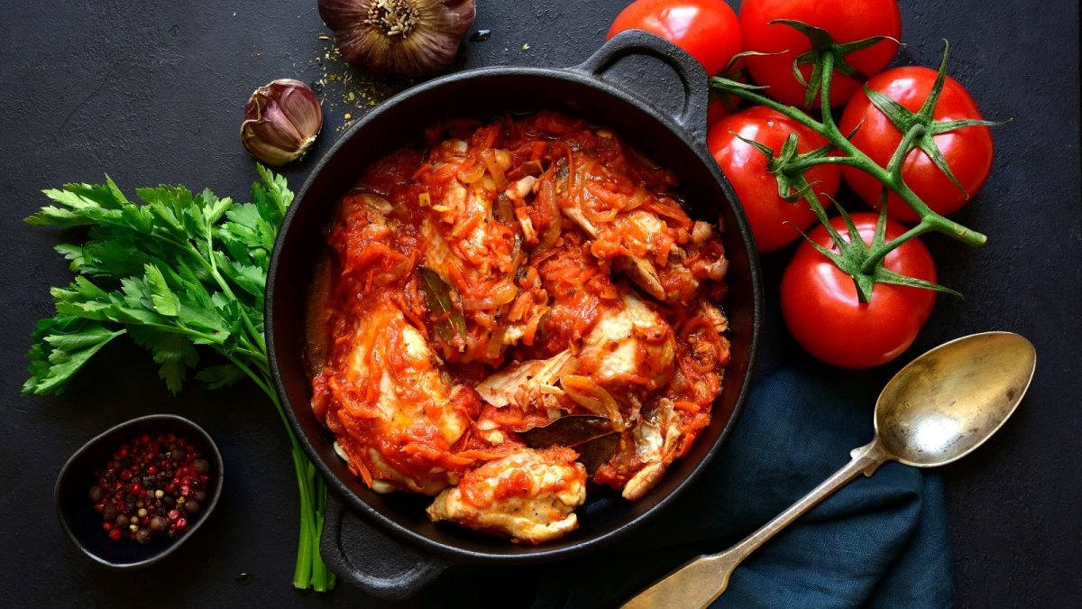 Ein schwarzer Topf mit Chakhokhbili auf einem schwarzen Tisch neben frischen Tomaten