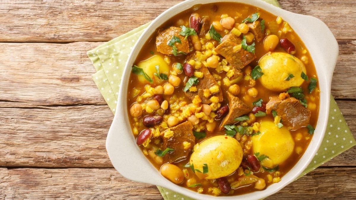 Ein runder Topf mit Cholent Hamin auf einem Holztisch.