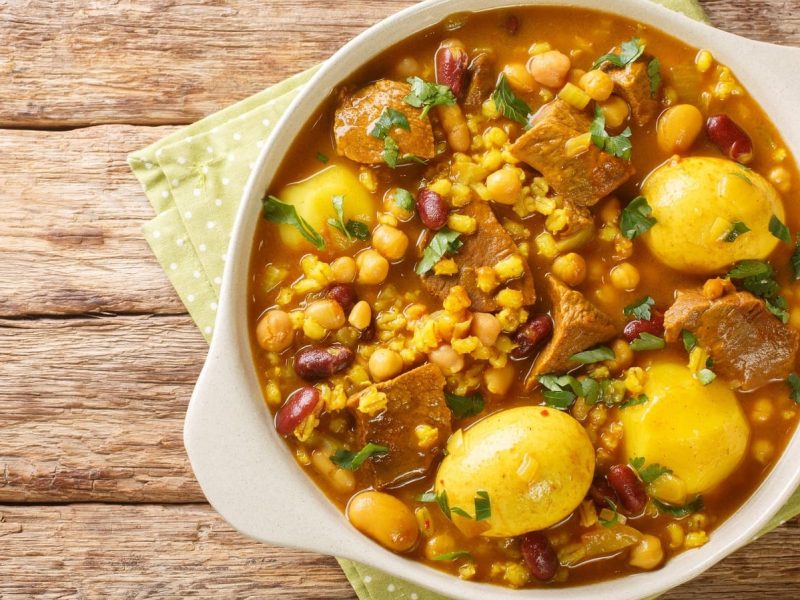 Ein runder Topf mit Cholent Hamin auf einem Holztisch.