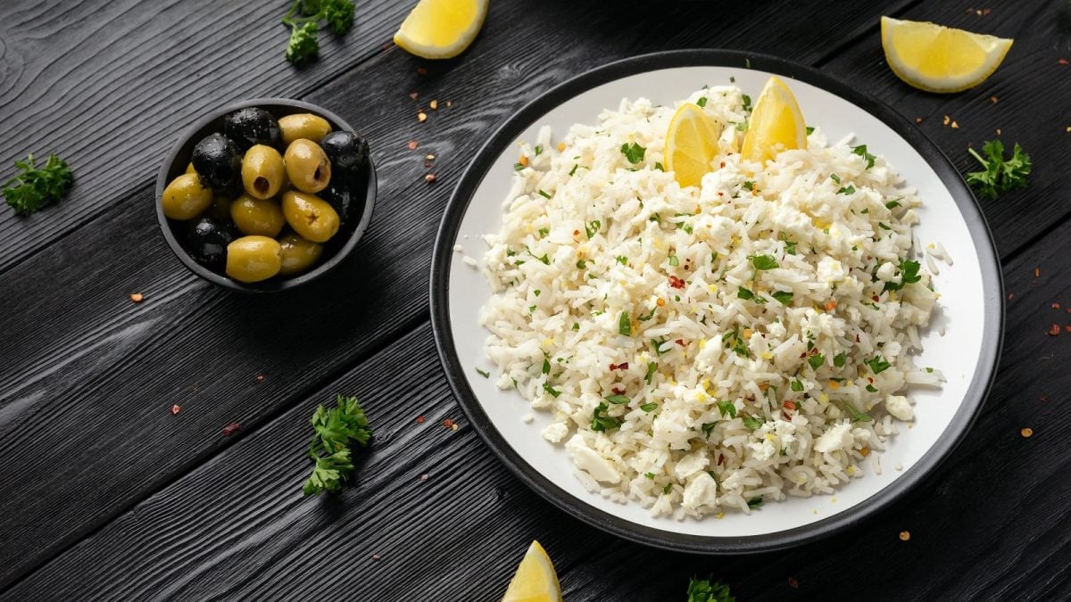 Ein weißer Teller mit Feta-Reis mit Zitrone auf einem dunklen Tisch.
