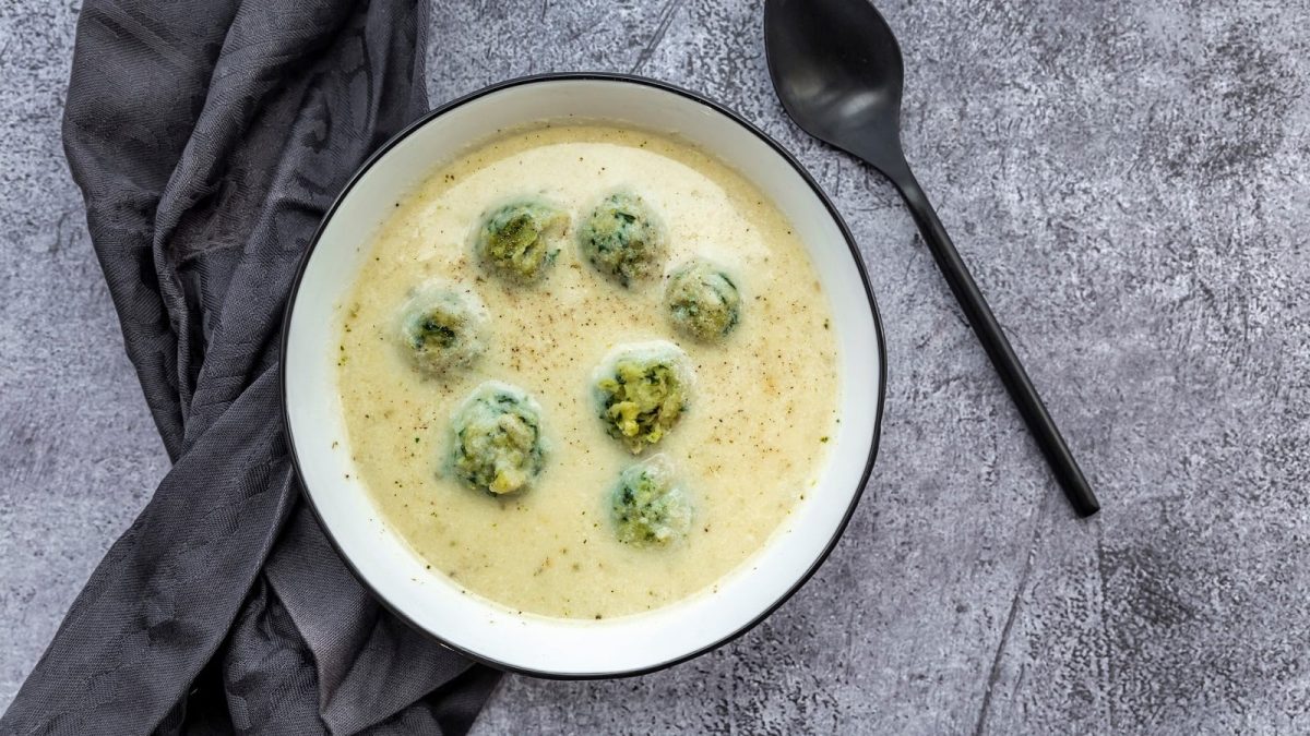 Eine runde Schüssel gefüllt mit Kohlrabi-Cremesuppe neben einem grauen Geschirrtuch.