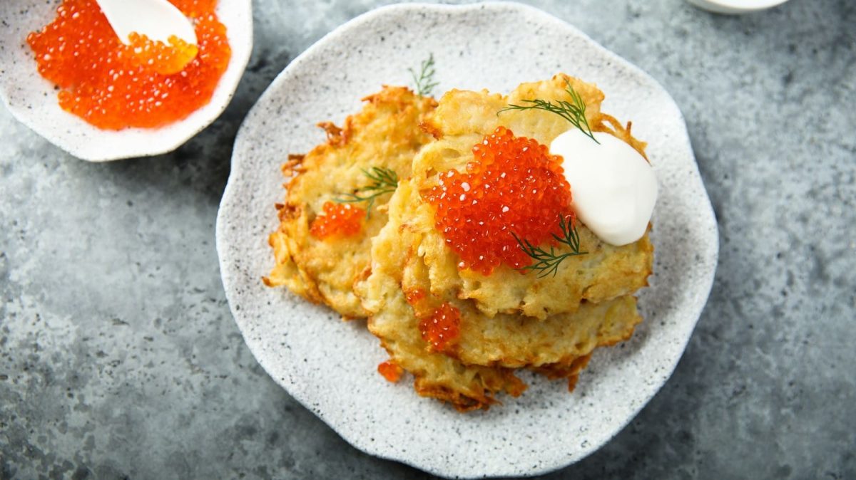Ein weißer Teller mit Latkes auf einem grauen Tisch.