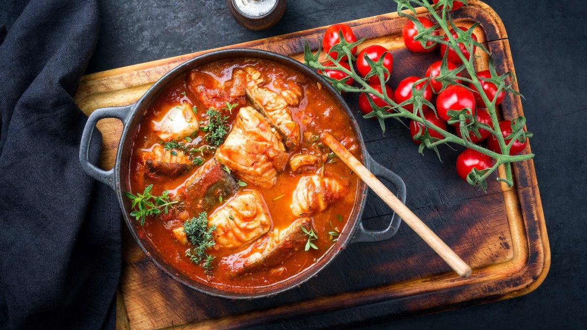Ein schwarzer Topf mit Moqueca Baiana auf einem Holzbrett.