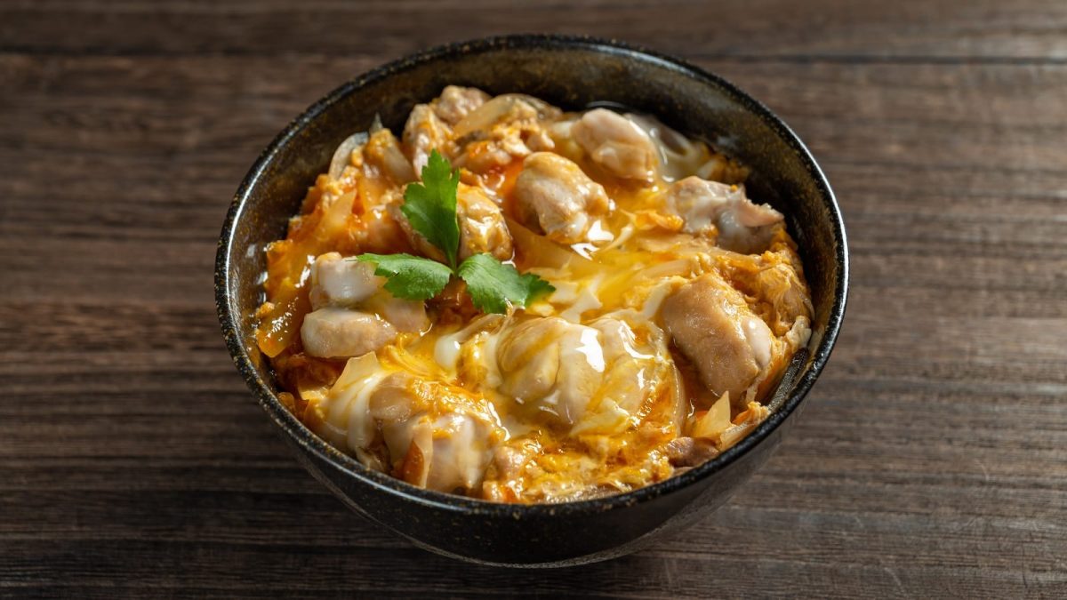 Eine schwarze Schüssel mit Oyakodon auf einem dunklen Tisch.