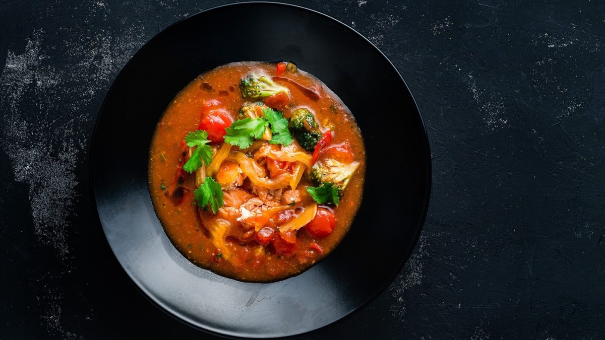 Eine schwarze Schüssel auf einem dunklen Tisch mit vietnamesischer Gemüsesuppe mit Lachs.