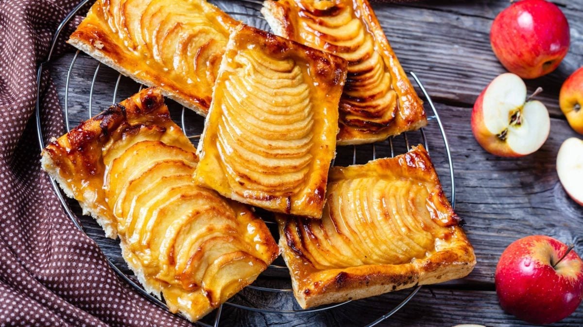Apfel-Marzipan-Tarte aus der Serie Emily in Paris auf Schieferplatte. Daneben Äpfel. Draufsicht.
