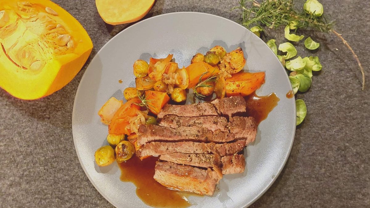 Ein grauer Teller mit dem Fleisch udn gemüse auf dunkelgrauem Untergrund.