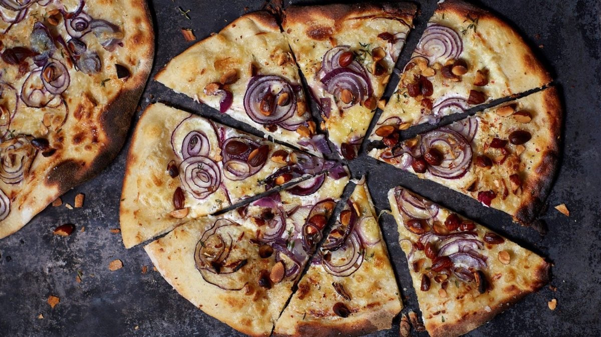 Ein geschnittener Flammkuchen mit Räuchermandeln und roten Zwiebeln.