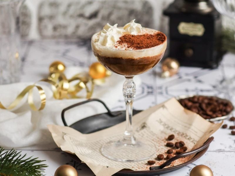Ein hohes Glas mit dem Hot White Russian auf einem weißen Tisch mit Kaffeebohnen.