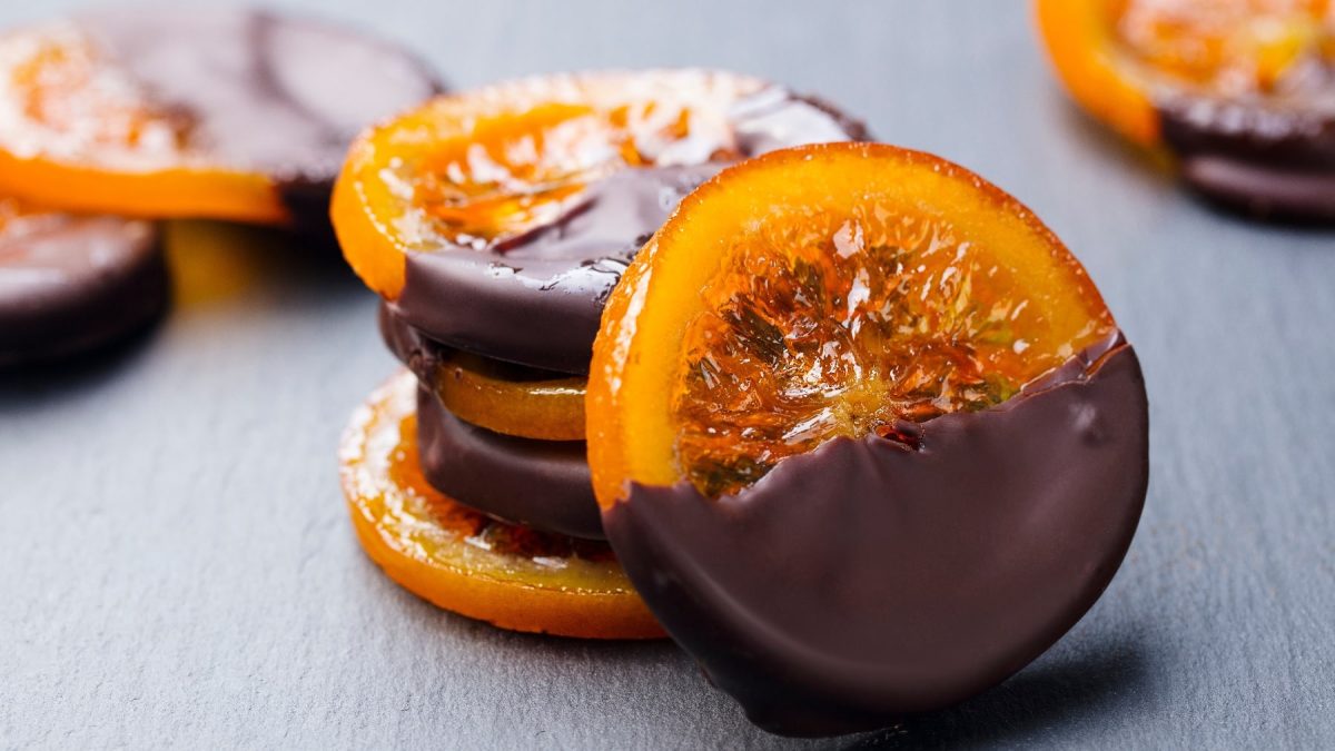 Ein paar der kandierten Orangenscheiben mit Schokolade auf eine rschwarzen Schieferplatte.