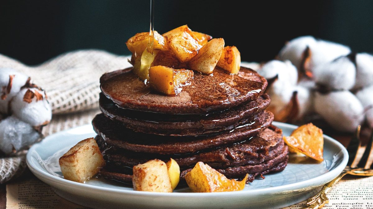 Ein Stapel Lebkuchen-Pancakes mit gebackenen Apfelstückchen und Sirup auf einem Teller.