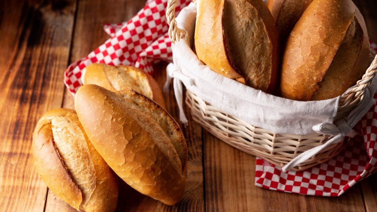Original mexikanische Bolillos Brötchen wie Baguette in einem Korb mit rot-weißem Tuch auf Holztisch. Daneben weitere Bolillos. Draufsicht.