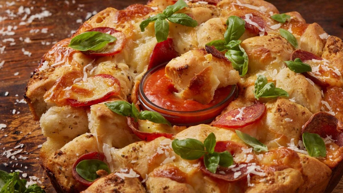 Peperoni Pull Apart Monkey Bread mit Marinara-Dip in der Mitte auf Holz. Draufsicht.