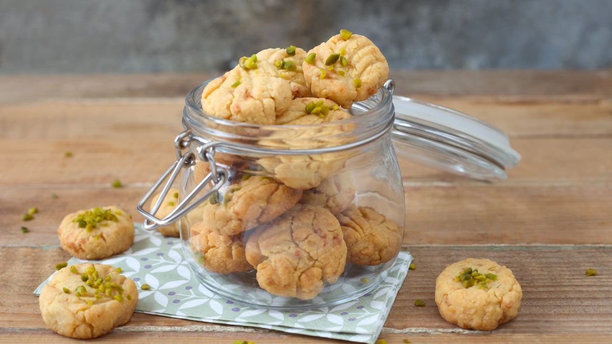 Ein offenes Glas Pistazien-Plätzchen auf einer Serviette, daneben liegen ein paar Plätzchen.