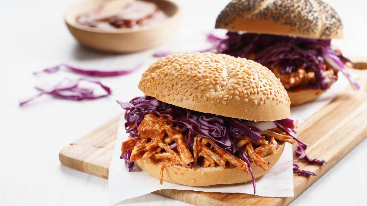 Zwei der Pulled Chicken Burger auf einem Holzbrett und hellem Untergrund.