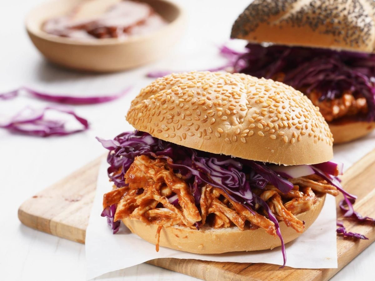 Zwei der Pulled Chicken Burger auf einem Holzbrett und hellem Untergrund.