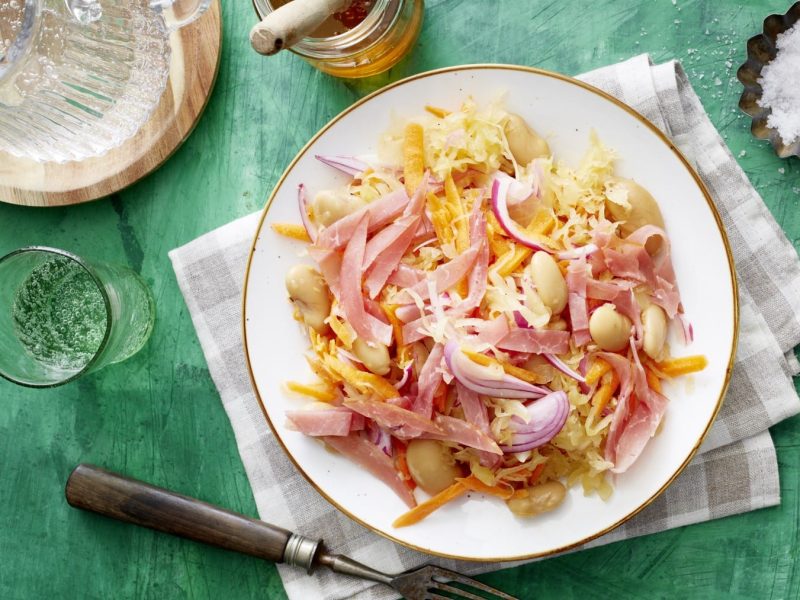 Sauerkraut-Salat mit weißen Bohnen auf einem weißen Teller mit grünem Hintergrund in der Draufsicht.