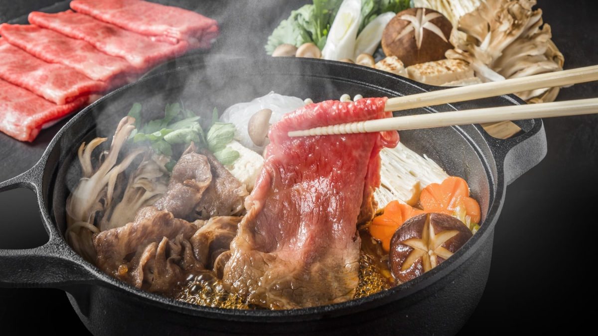 Eine schwarze Schale mit dem Shabu-Shabu. Im Hintergrund viele verschiedene Zutaten und ein schwarzes Brett mit dem Fleisch.