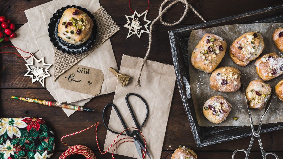 Stollenkonfekt mit Marzipan und selbst eingelegten Rumrosinen auf Backblech. Im Bild Geschenkutensilien und Weihnachtsschmuck. Draufsicht.