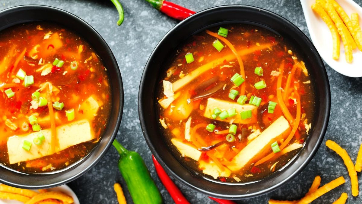 Zwei schwarze Schüsseln mit Sauer-Scharf-Suppe neben frischen Chilis.