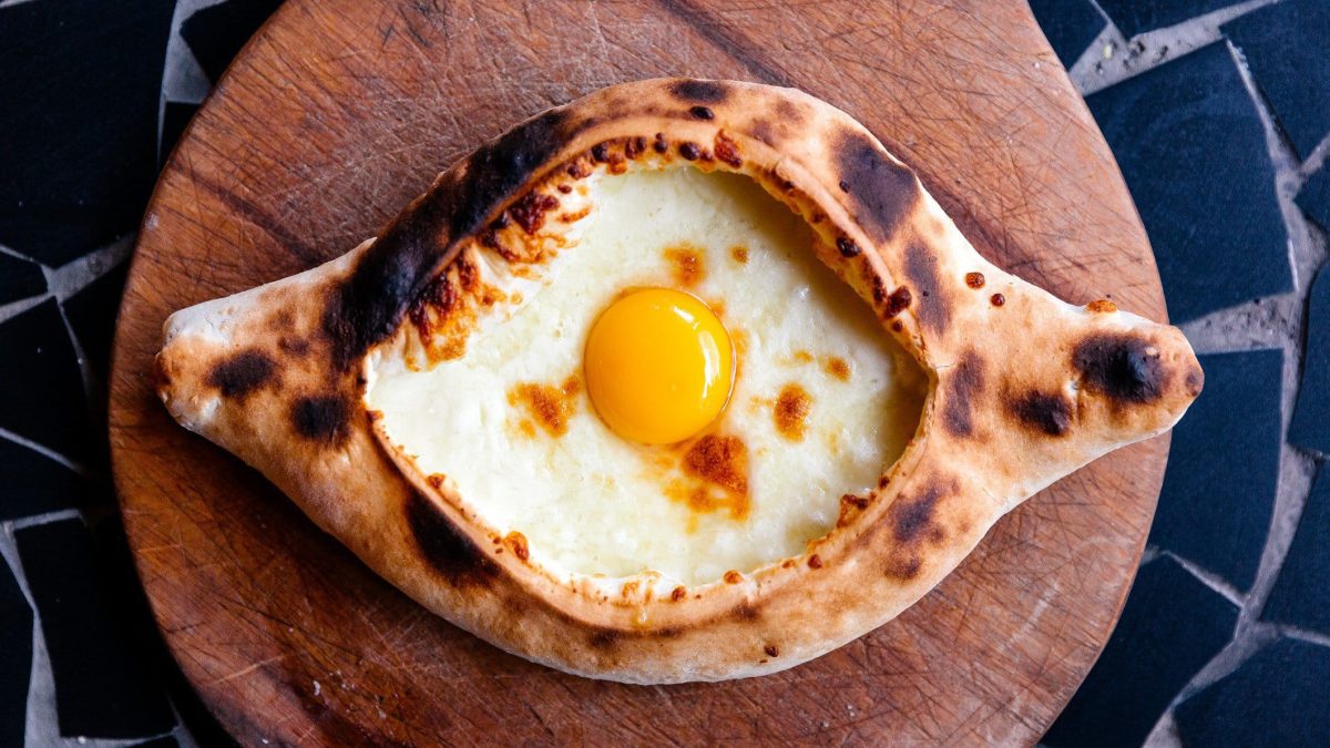 Khachapuri oder CHatschapuri mit Käse und Ei auf Holzbrett und Marmortisch. Draufsicht.
