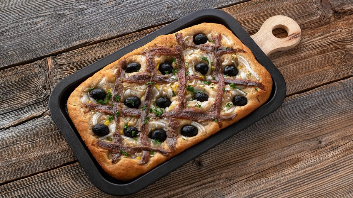 Ein schwarzes Blech mit dem Zwiebelkuchen auf einem rustikalen, dunklen Holztisch.