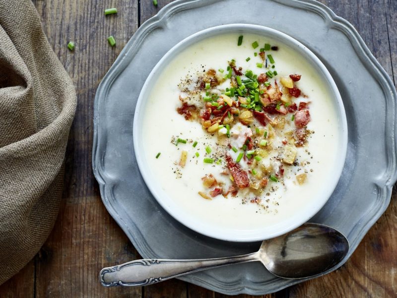 Selleriesuppe mit Apfel-Bacon-Salsa, garniert mit Schnittlauch und serviert in einer großen Suppenschale auf einem Holztisch.
