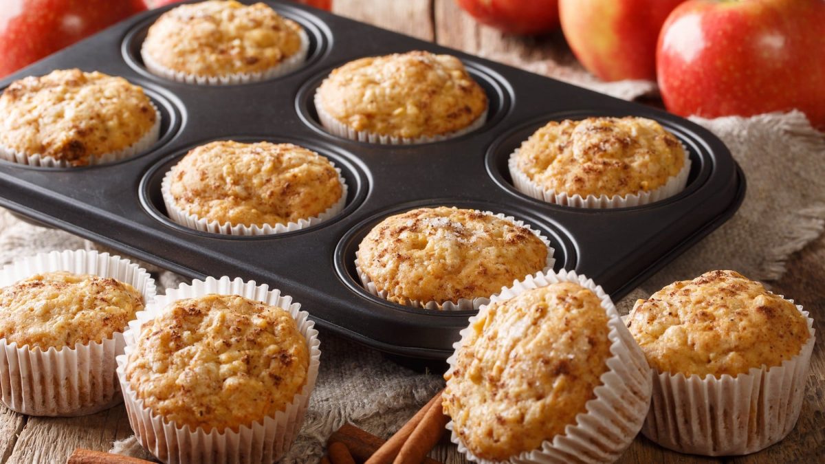 Ein Blech Apfelmus-Muffins, daneben ein paar weitere Muffins sowie Äpfel und Zimtstangen.