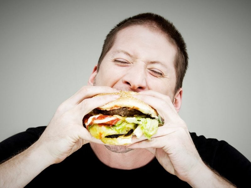 Burger essen ohne Kleckern japanische Methode mit dem Japan-Griff isst ein Mann einen Burger mit beiden Händen. Frontalansicht.