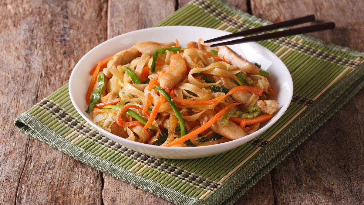 Chicken Chow Mein Chinesische Stir Fry Noodle mit schwarzen Essstäbchen in weißem Teller auf grünem Untersetzer und Holz. Draufsicht.