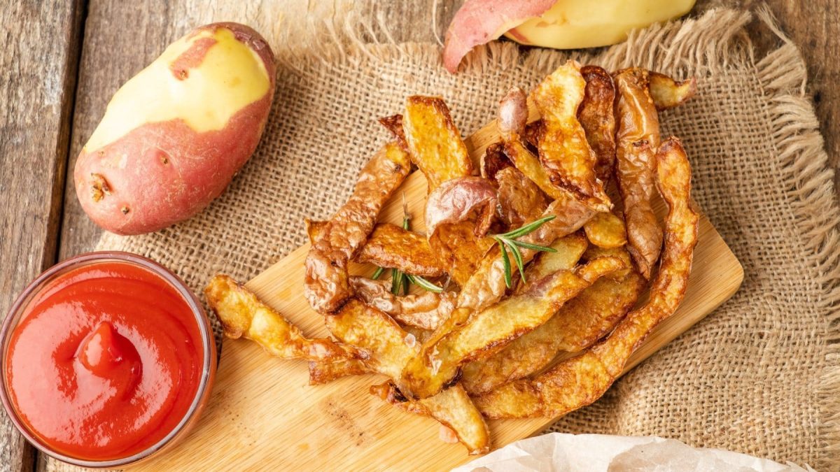 Chips aus Kartoffelschalen mit Kartoffeln und Ketchup auf Holzbrett auf einem Tuch. Draufsicht.