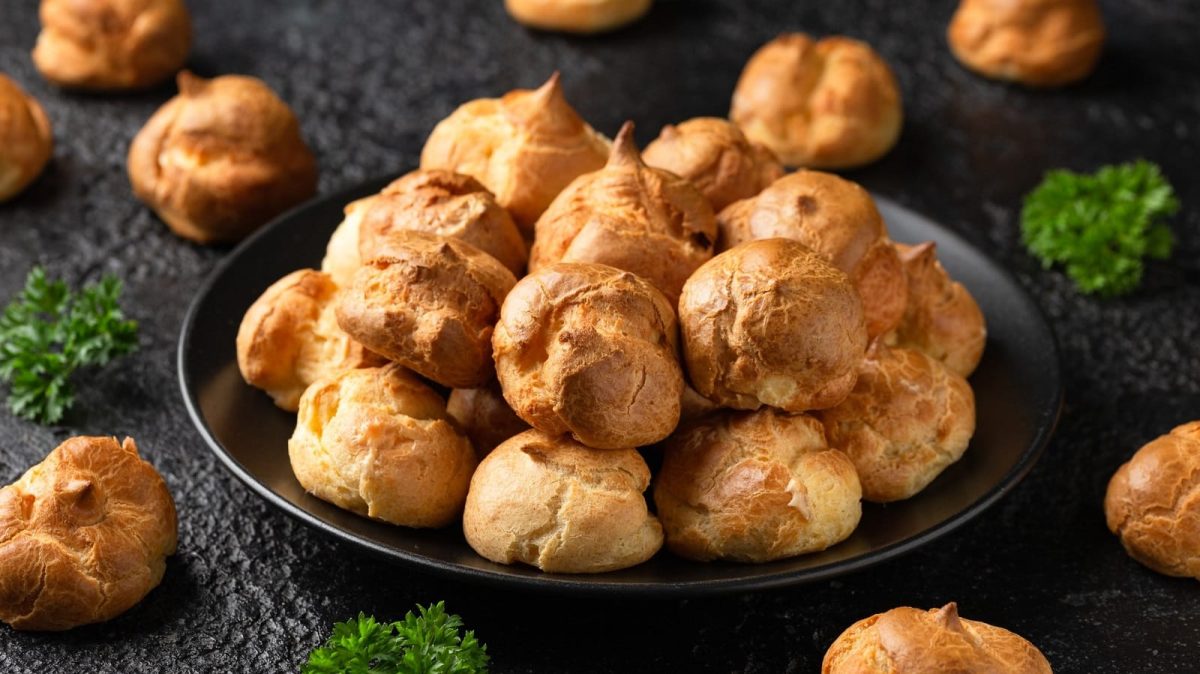 Ein schwarzer Teller mit Gougeres auf einem dunklen Tisch.