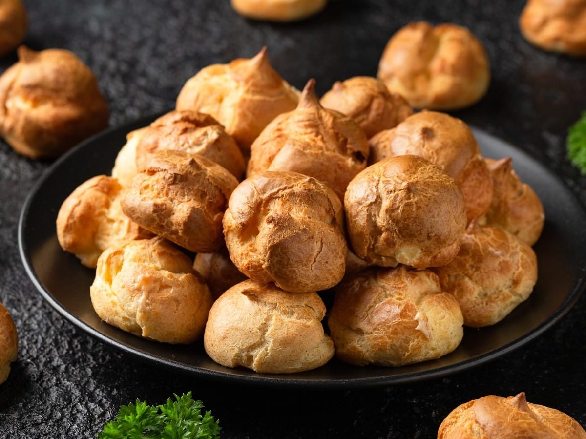 Ein schwarzer Teller mit Gougeres auf einem dunklen Tisch.