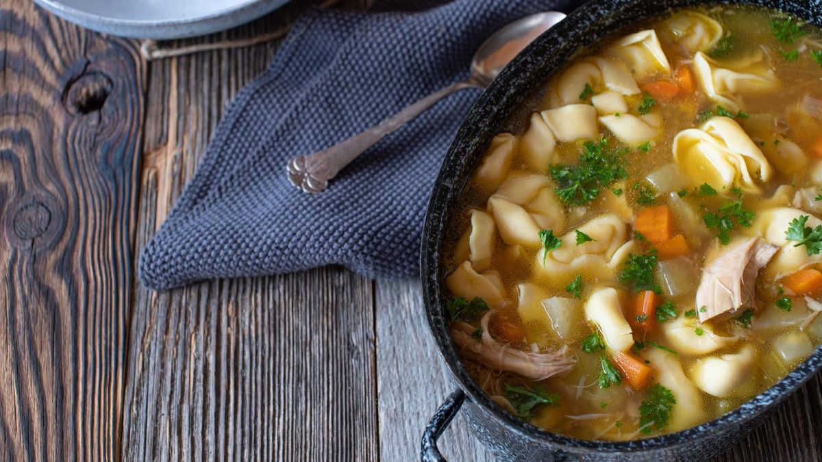 Ein Topf mit Hühnersuppe mit Tortelloni auf einem Holztisch.