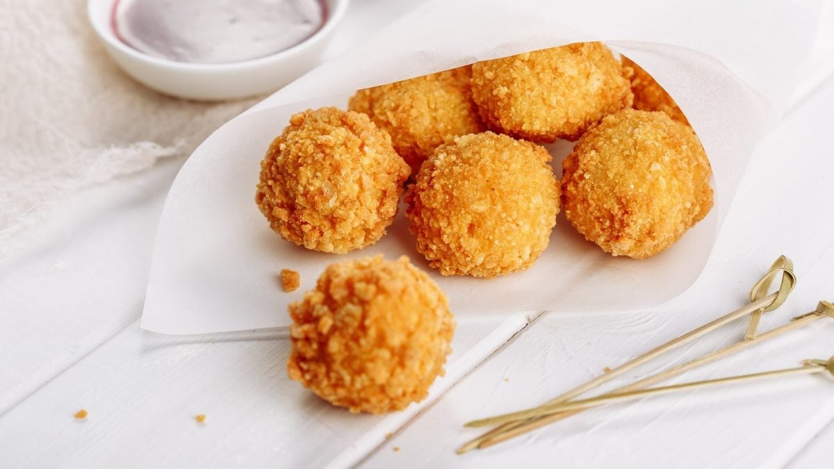 Eine weiße Papiertüte mit Käsebällchen neben Holzspießen.