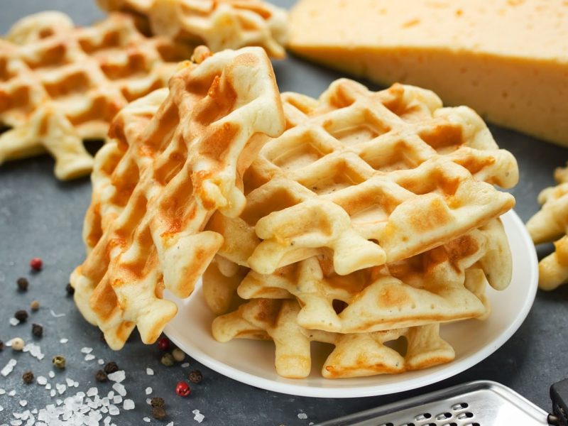 Ein Teller mit Käsewaffeln neben einem Block Käse.