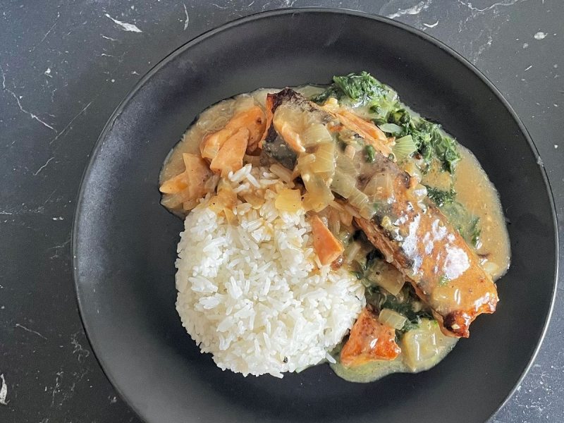 Ein schwarzer Teller mit Lachs auf Kokos-Spinatbett