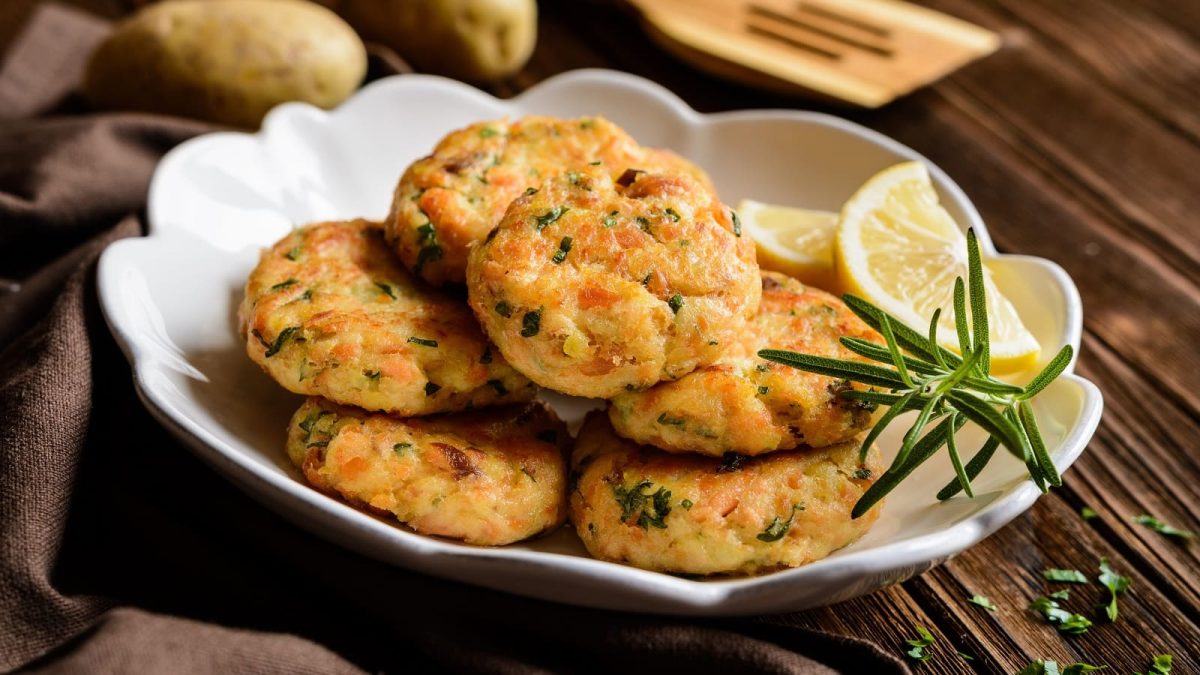 Ein Teller mit Lachs-Kartoffel-Bratlingen auf einem Holztisch.