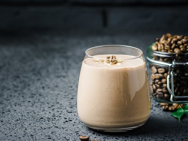 Ein Glas mit Peanut Butter Latte neben einem Glas mit Kaffeebohnen.