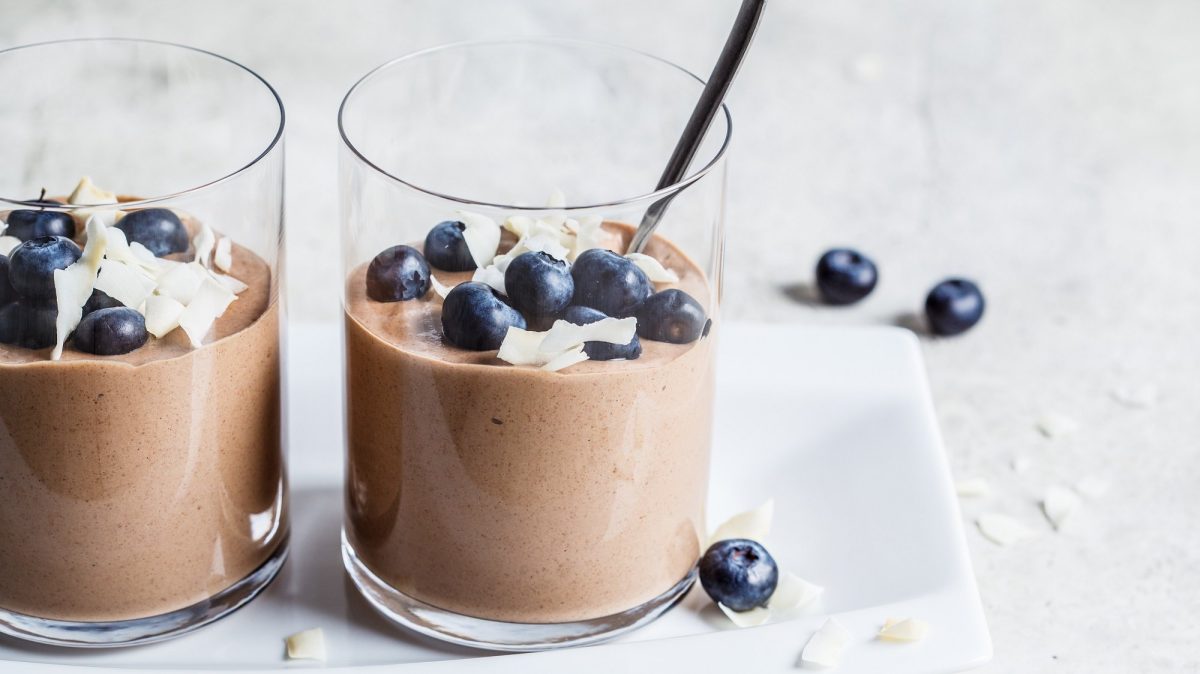 Zwei Gläser vegane Erdnussbutter-Mousse mit Blaubeeren und Kokosflocken, darin Teelöffel.