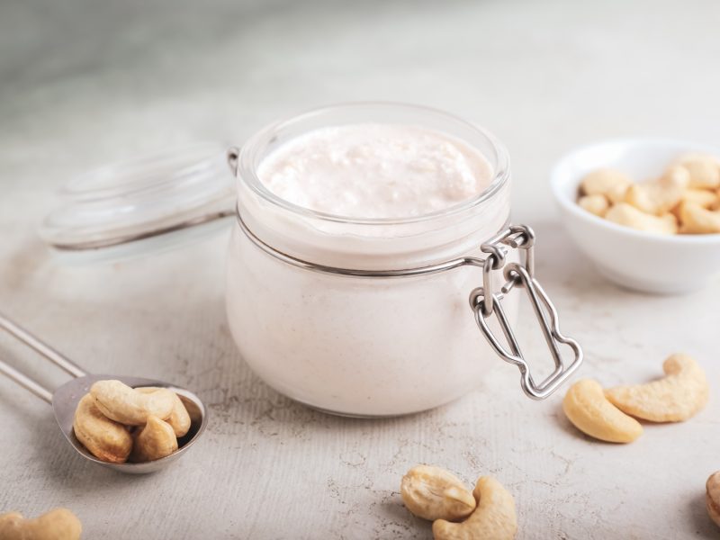 Totale von veganer Cashewsahne in einem Glas als Ersatz für Sahne aus Kuhmilch, daneben Cashewkerne.