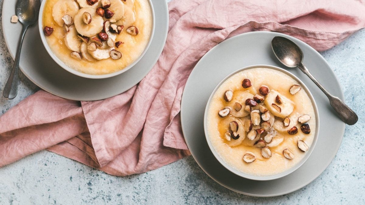 Zwei Schüsseln Frühstücks-Polenta mit karamellisieren Bananen und Haselnüssen in der Draufsicht.