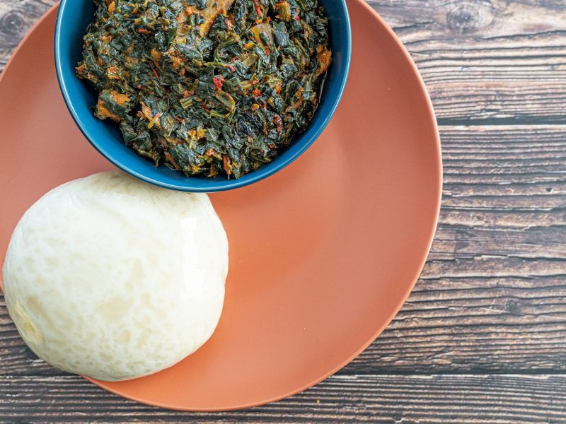 Fufu, ein afrikanischer Kloß, auf einem Teller mit einer Schüssel eines afrikanischen Gemüseeintopfes, Draufsicht.
