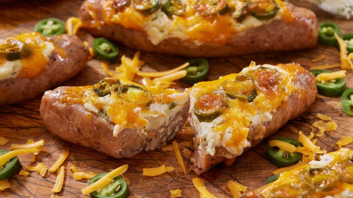 Zum Wintergrillen Gefüllte Salsiccia Knoblauchcreme, Cheddar und Jalapeño auf Holzbrett. Käse und Chilis im Bild. Frontalansicht.